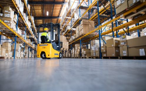 Young male worker lowering a pallet with boxes. Forklift driver working in a warehouse.